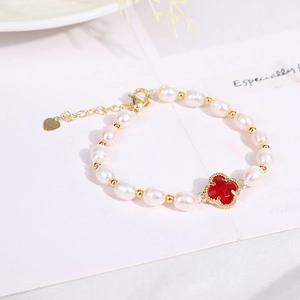 Detail of gold pearl bracelet featuring a red clover charm and heart tag on white paper