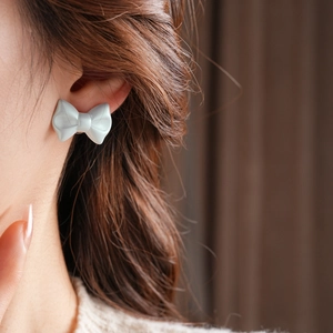 Close-up of minimalist light grey acrylic bow stud earring worn on the earlobe