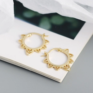 Close-up of golden hollow sun pattern earrings on a minimalist white card background