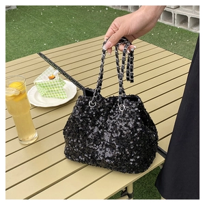 Detail of a sparkling black sequin bucket bag with silver metal chain on an outdoor table