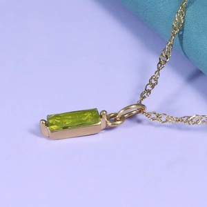 Close-up of golden necklace with rectangular yellow-green gemstone on twist chain