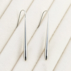 Close-up of polished silver stainless steel teardrop earrings on beige velvet display