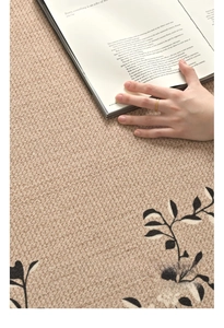 Close-up of a thin gold engraved ring worn by a model on a beige woven floral rug