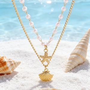 Collana a doppio strato con stella marina, conchiglia e perle su sfondo di spiaggia dorata