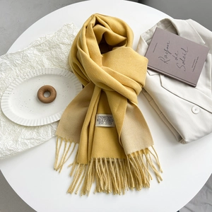 Detail of yellow and beige double-sided scarf with tassels and stitched brand label