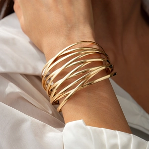 Detailansicht eines mehrlagigen goldenen Metallarmbands am Handgelenk des Models
