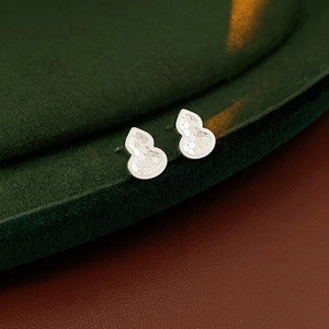 Close-up of silver gourd-shaped stud earrings with textured finish on green velvet