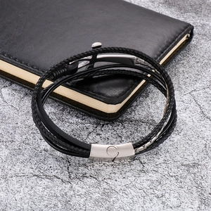Detail of multi-layer black leather bracelet with silver anchor clasp on a textured desk