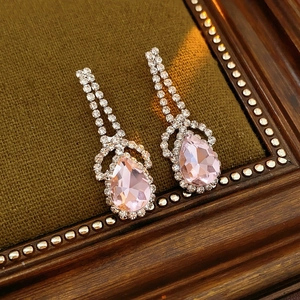 Close-up of pink crystal teardrop earrings with silver diamond setting on green velvet