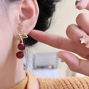 Close-up of model wearing sweet cherry-shaped drop earrings with dark red resin and gold stem