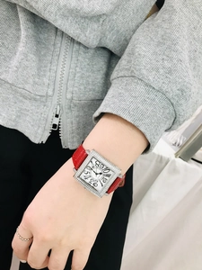 Detalle de caja de reloj cuadrada con diamantes y correa de cuero rojo en mano