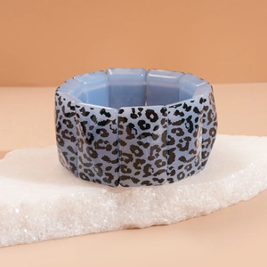 Detail of blue acrylic leopard print bracelet displayed on natural white stone base