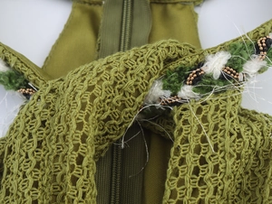 Close-up of olive green knit texture with gold beads, tassels and invisible zipper