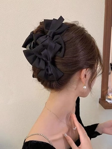 Detail of elegant black satin layered bow hair claw clip worn on hair bun for women