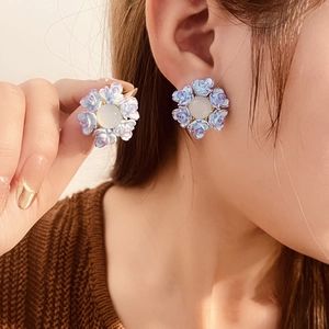 Close-up of floral resin earrings in pastel blue and purple tones worn on ear