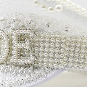 Dettaglio cappello da sposa con paillettes bianche, lettera E di perle e borchie punk