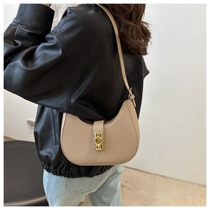 Beige crescent-shaped underarm bag with gold metal buckle and adjustable strap on a model