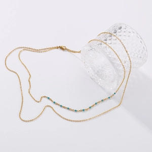 Détail d'un collier à double chaîne dorée avec petites perles vertes sur un verre