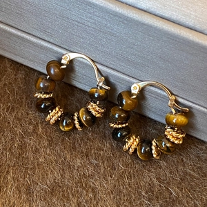 Macro detail of tiger eye beaded hoop earrings with gold twisted metal accents