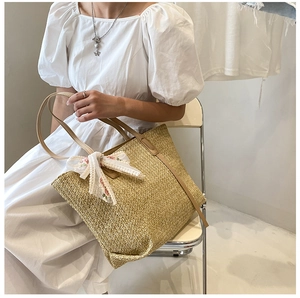 Khaki straw tote bag with floral silk bow detail carried by a model in a summer dress