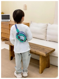 Kid wearing a car-shaped green chest bag with 'Brave' print in a home setting
