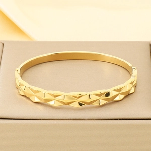 Detail view of gold wave knot bracelet showing fine geometric diamond cut surface