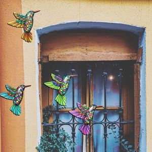 Set of four colorful mosaic hummingbird wall art pieces decorating an old yellow garden wall