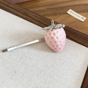 Detail view of a pink flocked strawberry hair clip with silver leaves on a wood tray