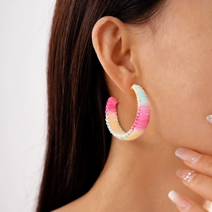 Detail of colorful woven C-shaped hoop earrings on model featuring a boho summer vibe