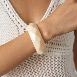 Close-up of a cream acrylic faceted geometric bangle worn with a white knit sweater