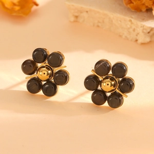 Detailed view of floral gold earrings with black cat-eye stone on elegant beige background