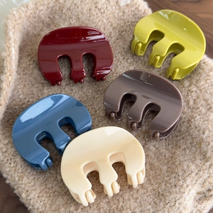 Flat lay of five acrylic M-shaped hair claws in assorted colors on soft fabric texture