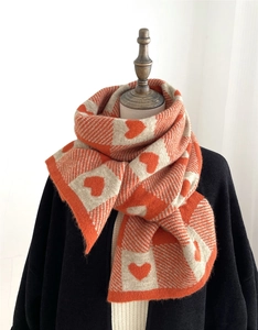 Detail of soft knitted scarf featuring orange and cream heart patterns on a mannequin