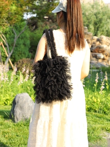 Detail of black ruffled tulle shoulder bag with pleated lace texture on model