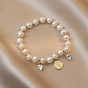 Detail of baroque freshwater pearl bracelet with gold coin pendant on silk background