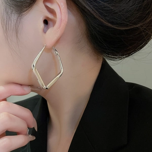 Close-up of a silver geometric rhombus earring on a model in professional attire