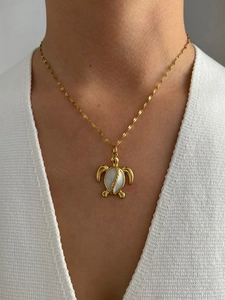 Close-up of a gold turtle pendant necklace with white enamel inlay worn on a neck