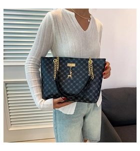 Detail of black tote bag with geometric pattern, gold deer charm and chain strap