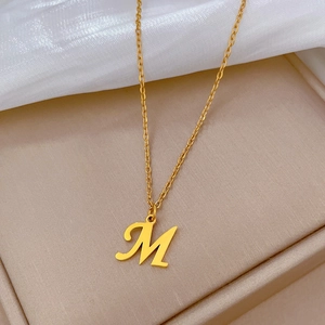 Detail of gold letter M pendant necklace on silk fabric inside a jewelry box