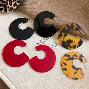 Detail of C-shaped acrylic earrings in black, marble red, and tortoiseshell patterns