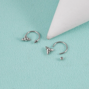 Macro detail of silver horseshoe lip rings with spikes and removable ball on teal surface