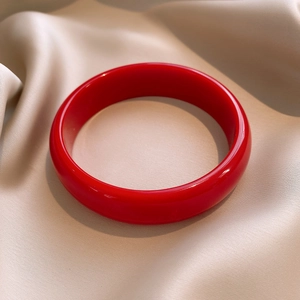 Close-up of a glossy red resin bangle on elegant champagne silk fabric texture