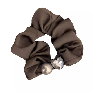 Detail of a brown satin scrunchie featuring a white pearl and a faceted heart-shaped gem