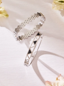 Close-up of silver hollow geometric bangles with black enamel inlay on a white surface
