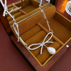 Gros plan d'un collier nœud argenté avec diamants et perle dans un coffret à bijoux en bois