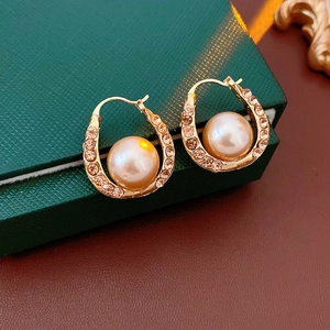 Detailed view of U-shaped gold earrings with large pearl and sparkling rhinestones