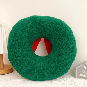 Detailed view of green Sherpa wreath pillow with red bow in a cozy Christmas setting