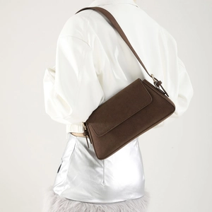 Side view of dark brown faux suede underarm bag styled on a model with white leather jacket