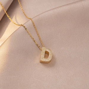 Macro detail of gold initial D pendant encrusted with white cubic zirconia on satin