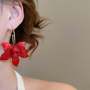 Close-up of model wearing large red resin flower pendant earrings with gold hoops